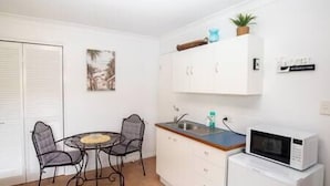 Una cocina compacta con comedor, armarios blancos, un microondas y una pequeña planta en maceta.