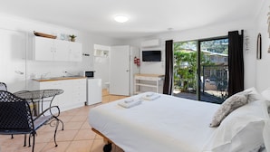Una habitación de hotel moderna con cama, una kitchenette pequeña, zona de comedor y balcón con vistas.