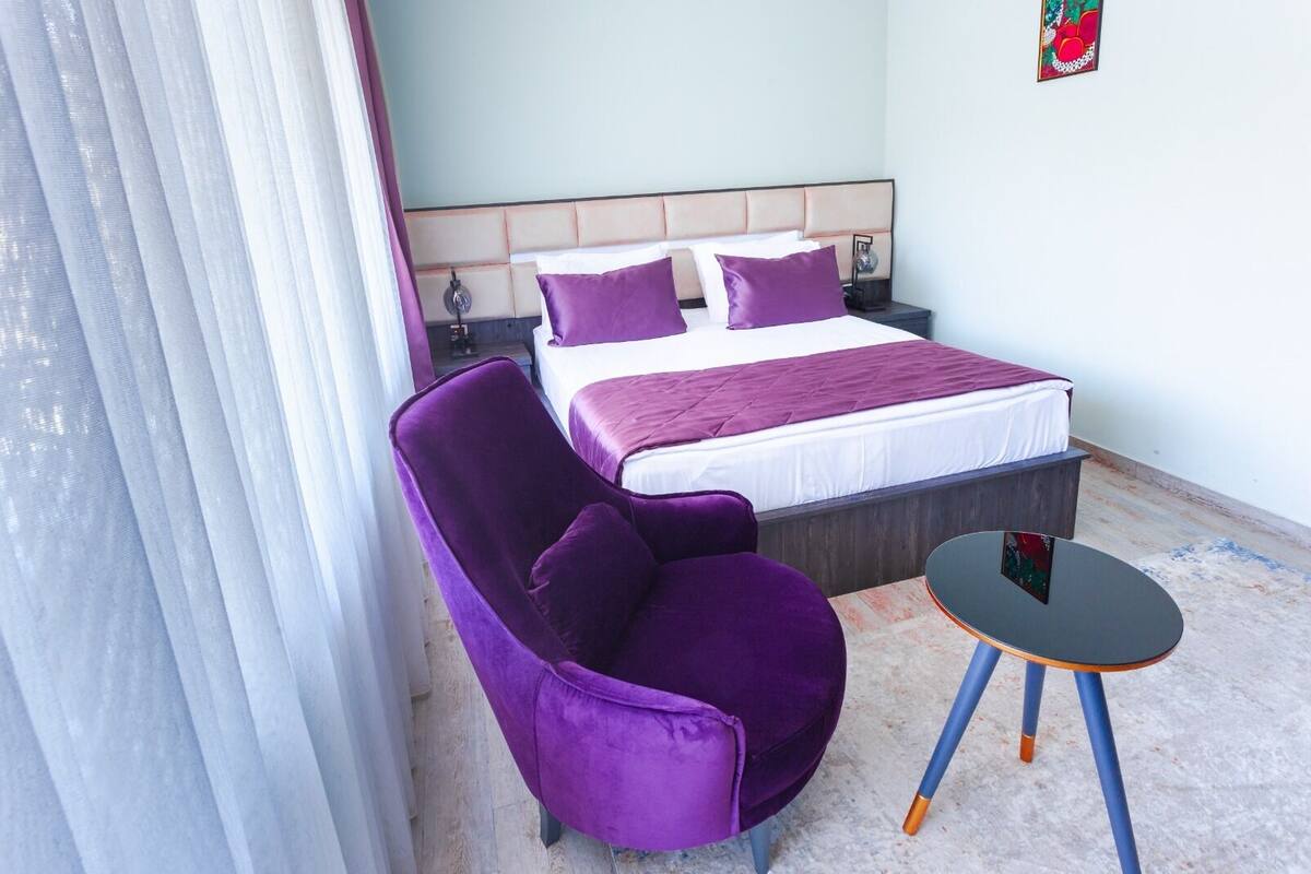 Een hotelkamer met een bed, een paarse fauteuil en een kleine tafel.