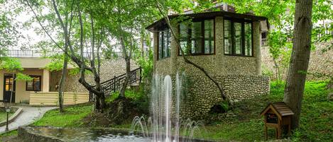 A stone building with a water fountain, surrounded by trees and a small pond.