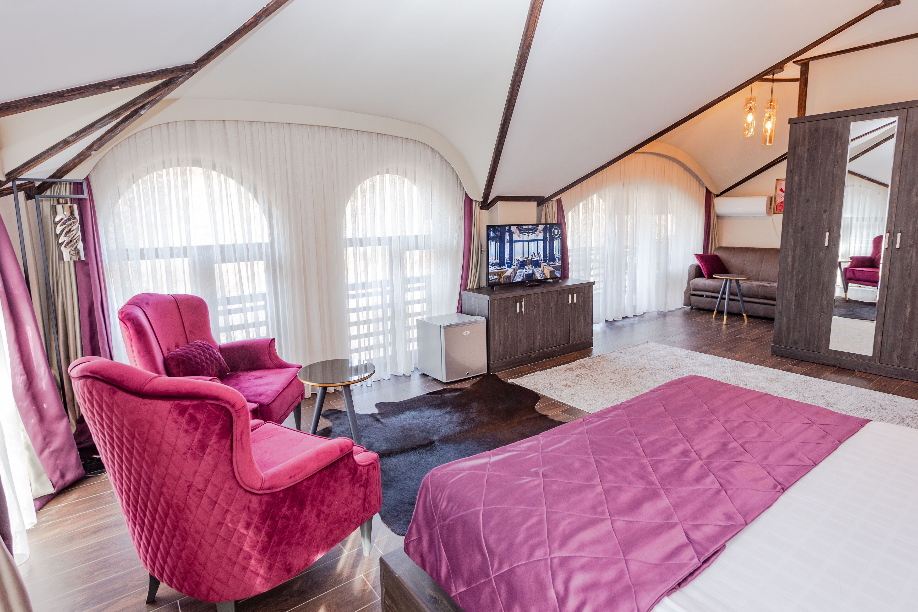 Ein geräumiges Zimmer mit einem großen Bett, einem roten Sessel, einem kleinen Tisch und einem Fernseher.