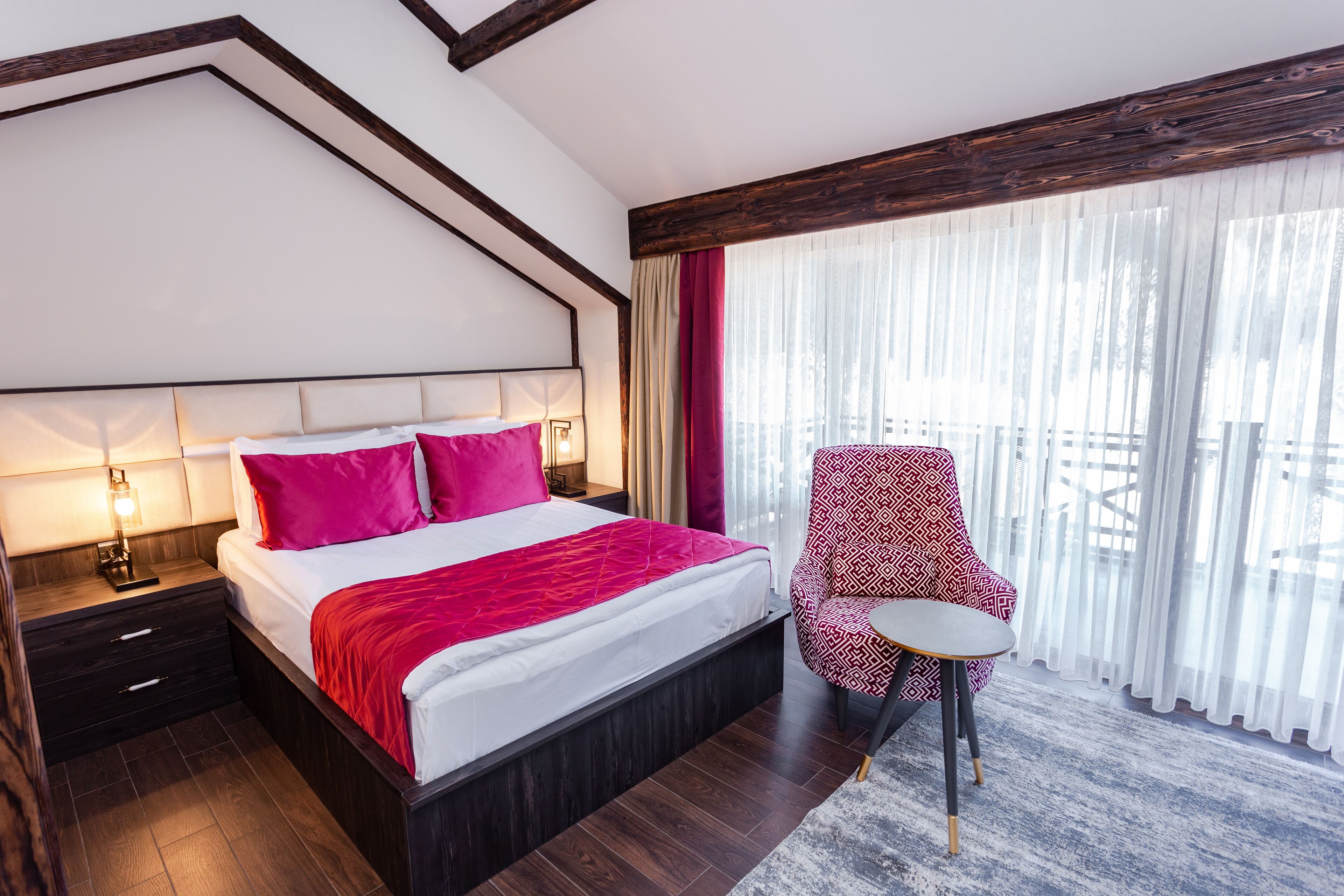 Ein modernes Hotelzimmer mit einem großen Bett, einem Nachttisch, einem Sessel und einem Balkon mit Vorhängen.
