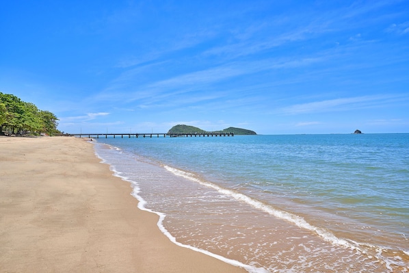 Enjoy a serene beach experience with a tranquil setting, a sandy beach, and a wooden pier extending into the sea.