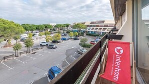 A view of a parking lot with several cars, a building with a red banner, and trees in the background. - Escale Port by Interhome (Port Camargue)