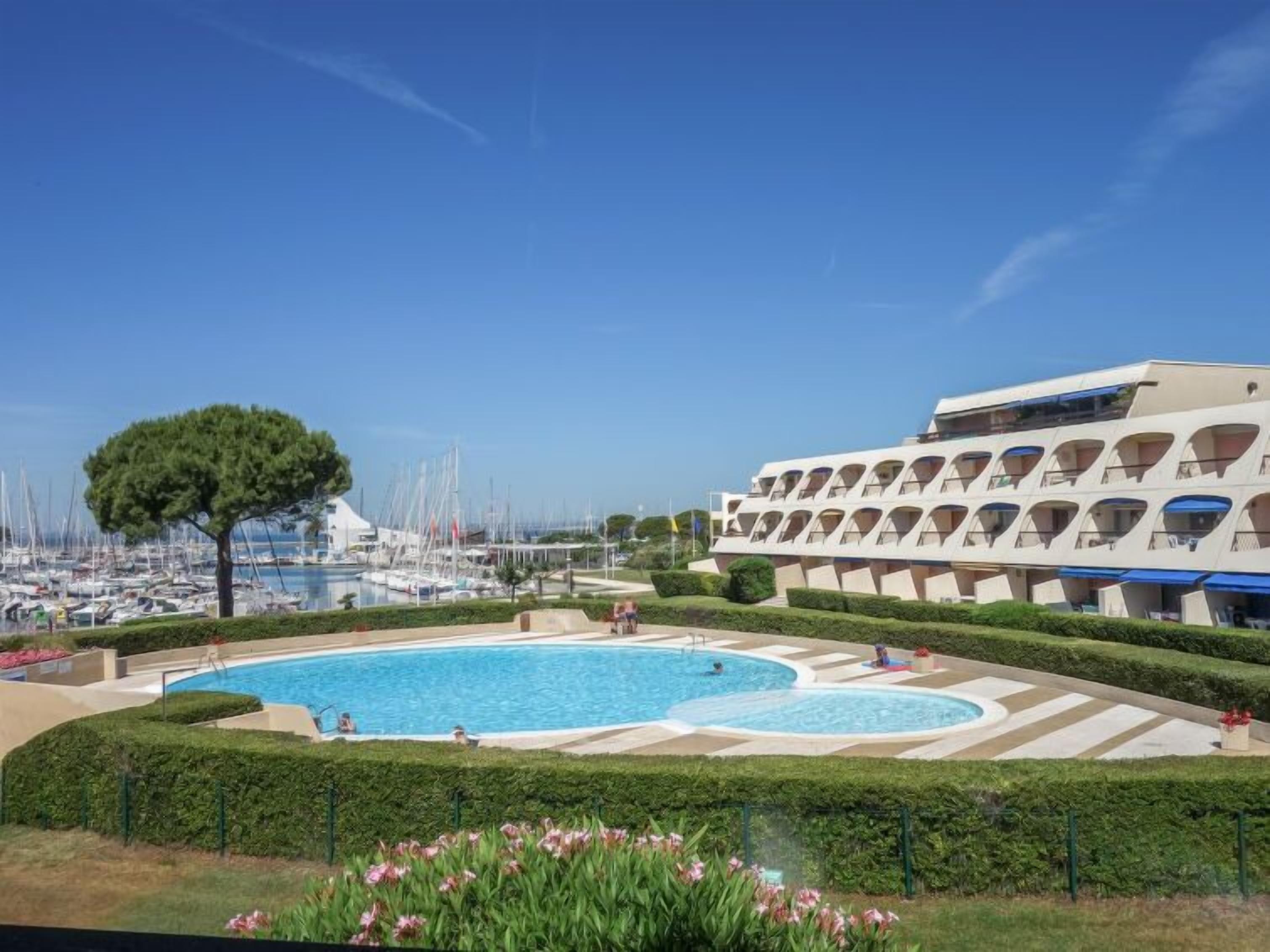 Ein Hotel mit Poolbereich, einer Marina voller Boote und blauem, wolkenlosem Himmel.