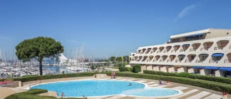 A hotel with a pool area, a marina with boats, and a clear blue sky.