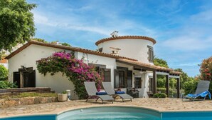 Area piscina con lettini, un patio coperto e un edificio con facciata bianca e tetto in tegole rosse.