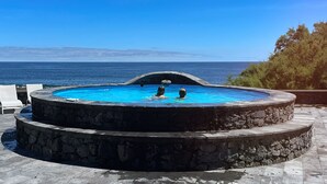 Ein kreisförmiger Infinity-Pool mit zwei Ebenen, umgeben von Steinstufen, mit Blick auf das klare, blaue Meer.