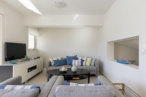Una sala de estar moderna con un sofá gris, una mesa de centro negra y un televisor de pantalla plana sobre un mueble blanco.