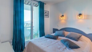 A bedroom with a bed, teal curtains, a view through a glass door, and two wall-mounted lights. - Les Restanques Golfe Saint Tropez by Interhome (Grimaud)