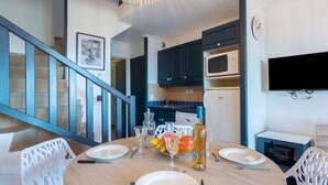 A dining area with a round table set for four, a staircase, and a kitchen with dark cabinets and a microwave. - Les Restanques Golfe Saint Tropez by Interhome (Grimaud)