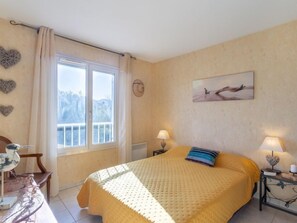 Une chambre à coucher avec un lit, deux lampes de chevet, une fenêtre avec des rideaux, une chaise et un tableau accroché au mur.