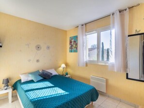 A bedroom with a bed, a nightstand, a lamp, a window with curtains, a radiator, and a wall with a floral pattern.