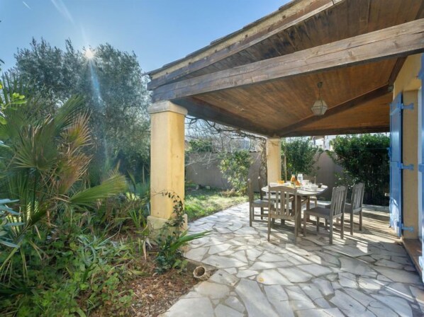 An outdoor patio with stone flooring, wooden furniture, and a pergola structure.