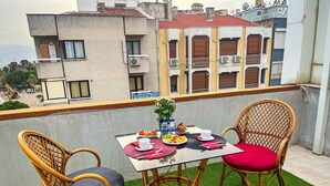 A balcony with a table set for two, featuring wicker chairs with cushions, a small potted plant, and a plate of food. - Life Artemis Otel (Izmir)