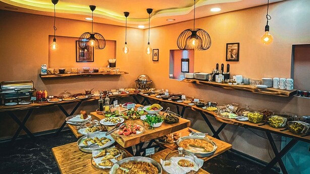 A restaurant with multiple tables set with various dishes, hanging pendant lights, and a marble floor. - Life Artemis Otel (Izmir)