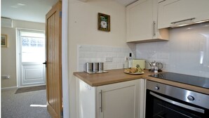 A kitchen with white cabinets, a wooden countertop, stainless steel appliances, and a clock on the wall. - Cosy Thatched Coastal Retreat, close to Maidencombe beach & beautiful pubs. (Stokeinteignhead Torquay)