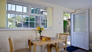 A dining area with a table set for two, a vase of yellow flowers, and breakfast items. - Cosy Thatched Coastal Retreat, close to Maidencombe beach & beautiful pubs. (Stokeinteignhead Torquay)