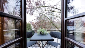 An outdoor patio with a table and chairs, a potted plant, and a view of trees and buildings.