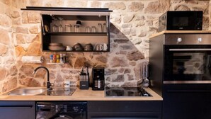 A compact kitchen with a stone wall, a built-in shelf with glassware, a coffee maker, and a dishwasher.