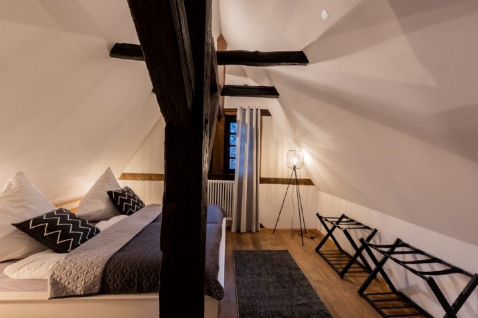 A cozy attic bedroom with a sloped ceiling, a bed with patterned pillows, a standing lamp, and a radiator.