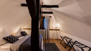 A cozy attic bedroom with a sloped ceiling, a bed with patterned pillows, a standing lamp, and a radiator.