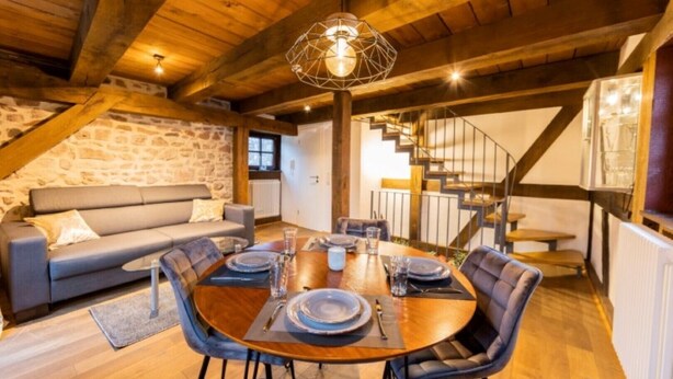 A cozy dining area with a wooden table set for four, a stone wall, and a staircase leading to an upper level.