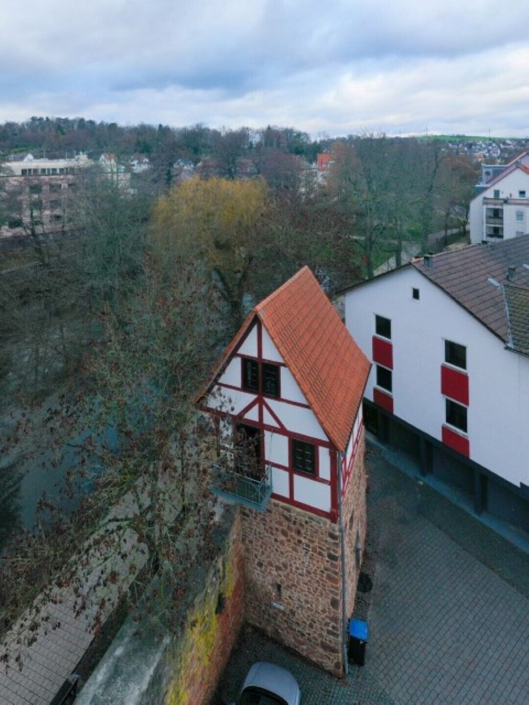 Une maison traditionnelle à colombages avec un toit rouge, située à côté d’un bâtiment moderne aux murs rouges et blancs.