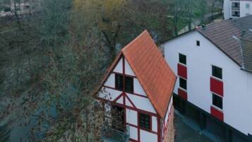 Une maison traditionnelle à colombages avec un toit rouge, située à côté d’un bâtiment moderne aux murs rouges et blancs.