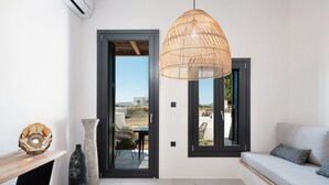A modern living room with a sofa, a wooden coffee table, a large woven pendant light, and a view through a glass door to an outdoor patio.