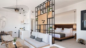 A modern, open-plan living space with a sofa, a dining area, and a bedroom with a bed and headboard.