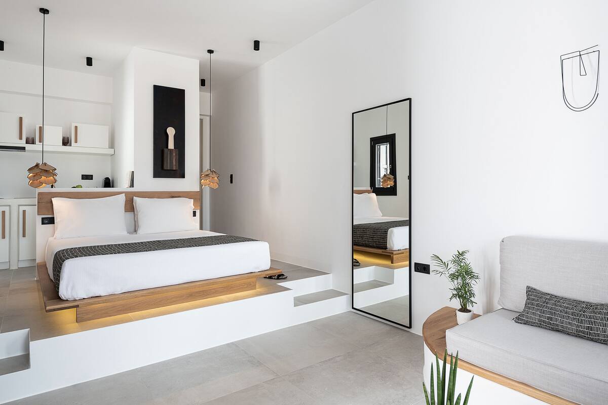 A modern bedroom with a bed, a large mirror, a sofa, and a potted plant.