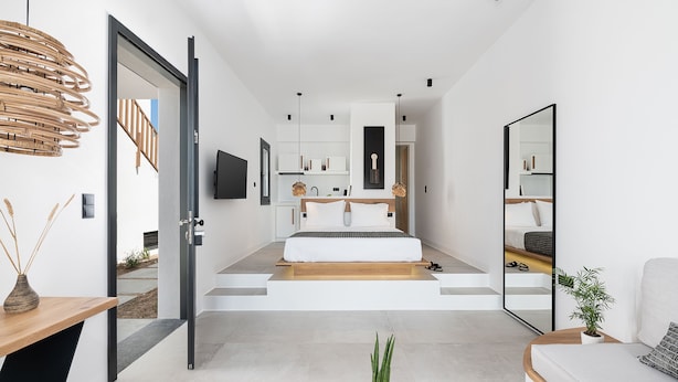 A modern bedroom with a large bed, a mirror, and a view of the outdoors.