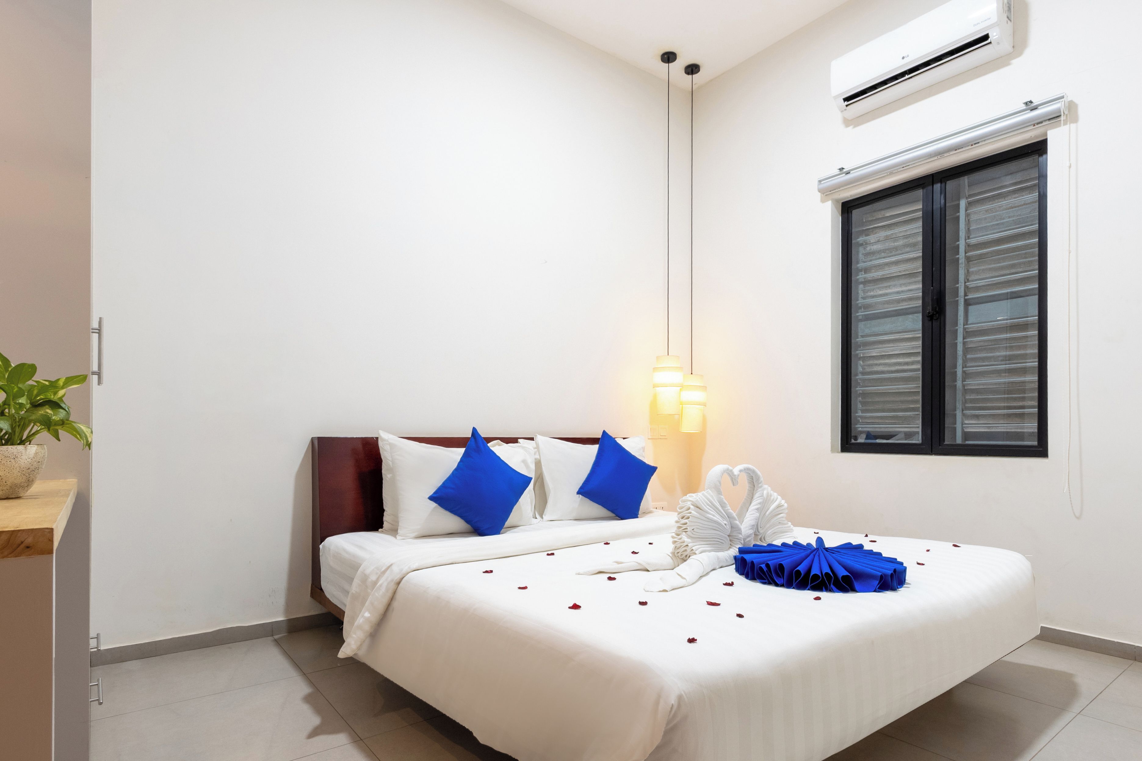 Ein Hotelzimmer mit Bett, Nachttisch, Wand-Klimaanlage und einem Fenster mit Jalousien.