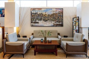 A modern lounge area with a sofa set, two armchairs, a coffee table, and a large painting of a cityscape. - Home-like Family/Group Stay in Three-Bedroom Suite- Near Pubstreet, Old Market (Krong Siem Reap)