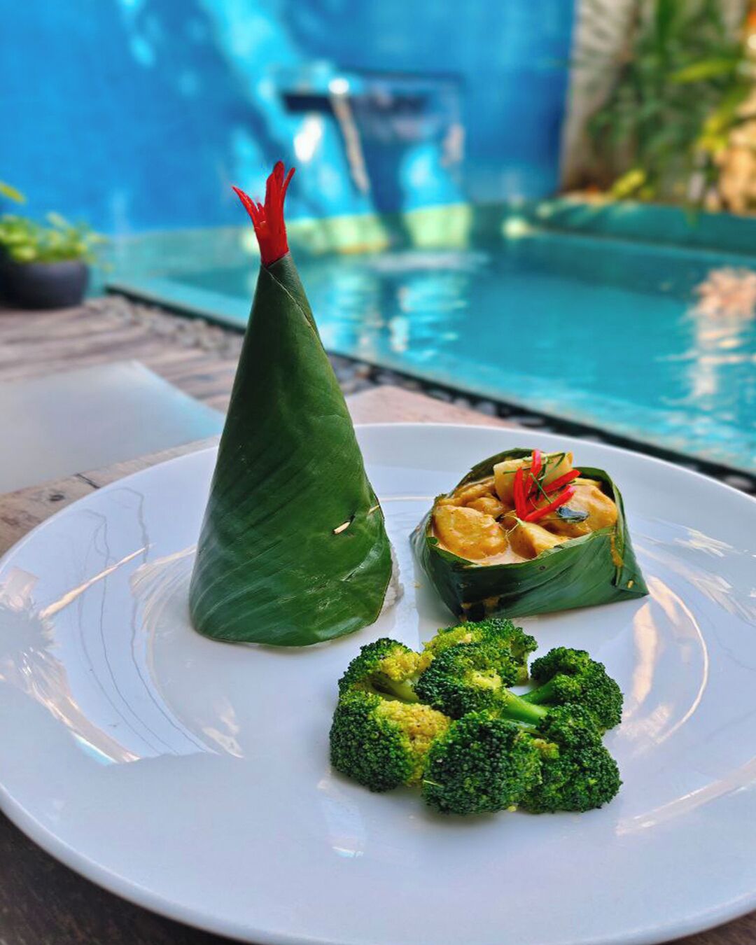 Un plato con un alimento envuelto, un trozo de brócoli y una piscina al fondo.