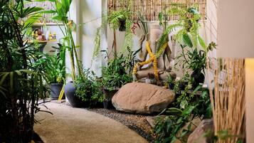 A well-maintained indoor garden with various plants, a large rock centerpiece, and a statue of a deity.