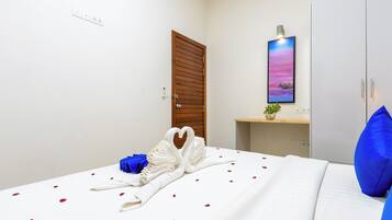 A hotel room with a bed, a wooden door, a painting, a small plant, and a blue pillow.