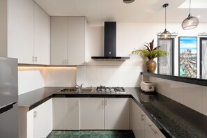 A modern kitchen with white cabinets, a black countertop, a gas stove, and a stainless steel refrigerator. - Home-like Family/Group Stay in Three-Bedroom Suite- Near Pubstreet, Old Market (Krong Siem Reap)