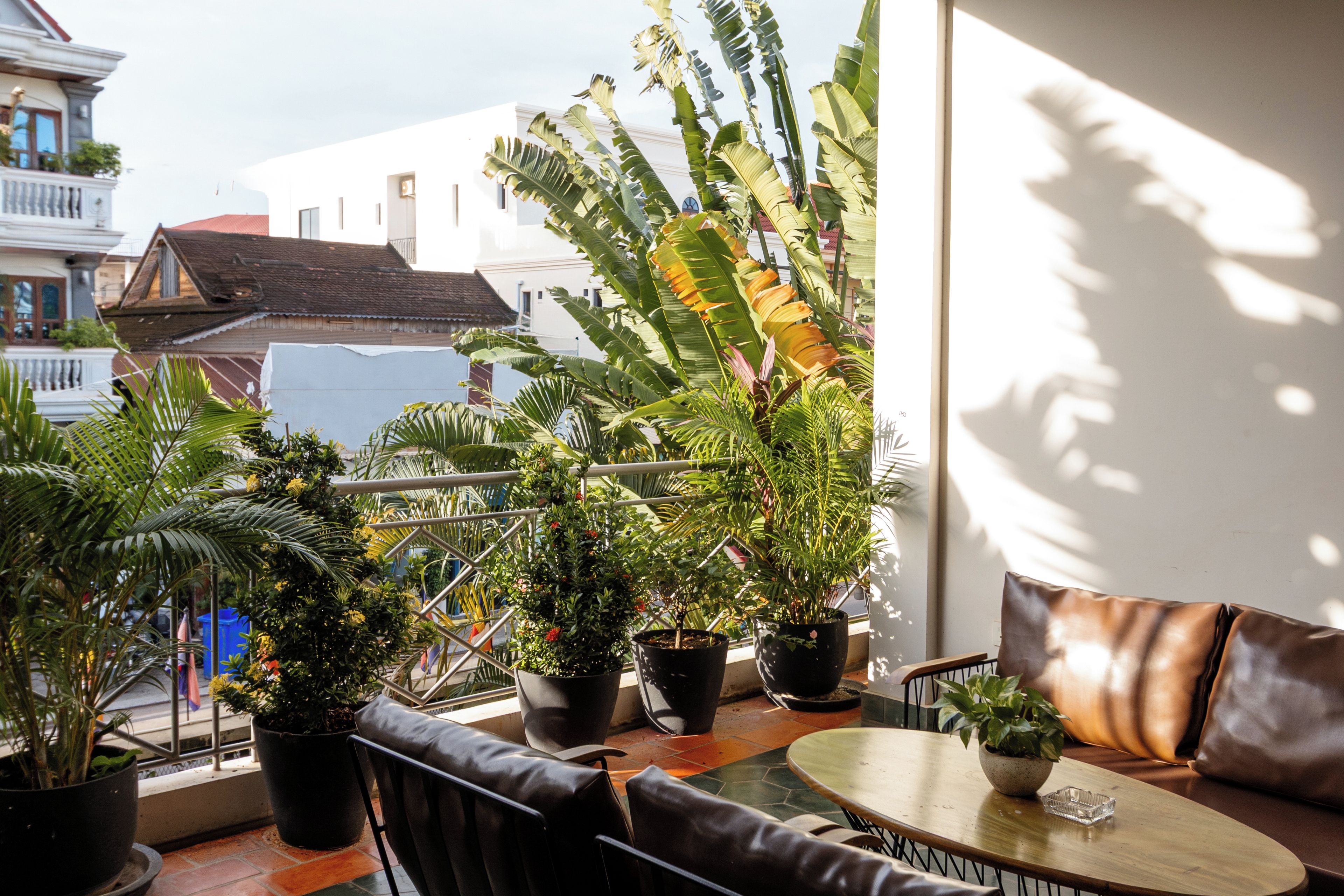 A balcony with potted plants, a seating area with a table and chairs, and a view of buildings in the background.