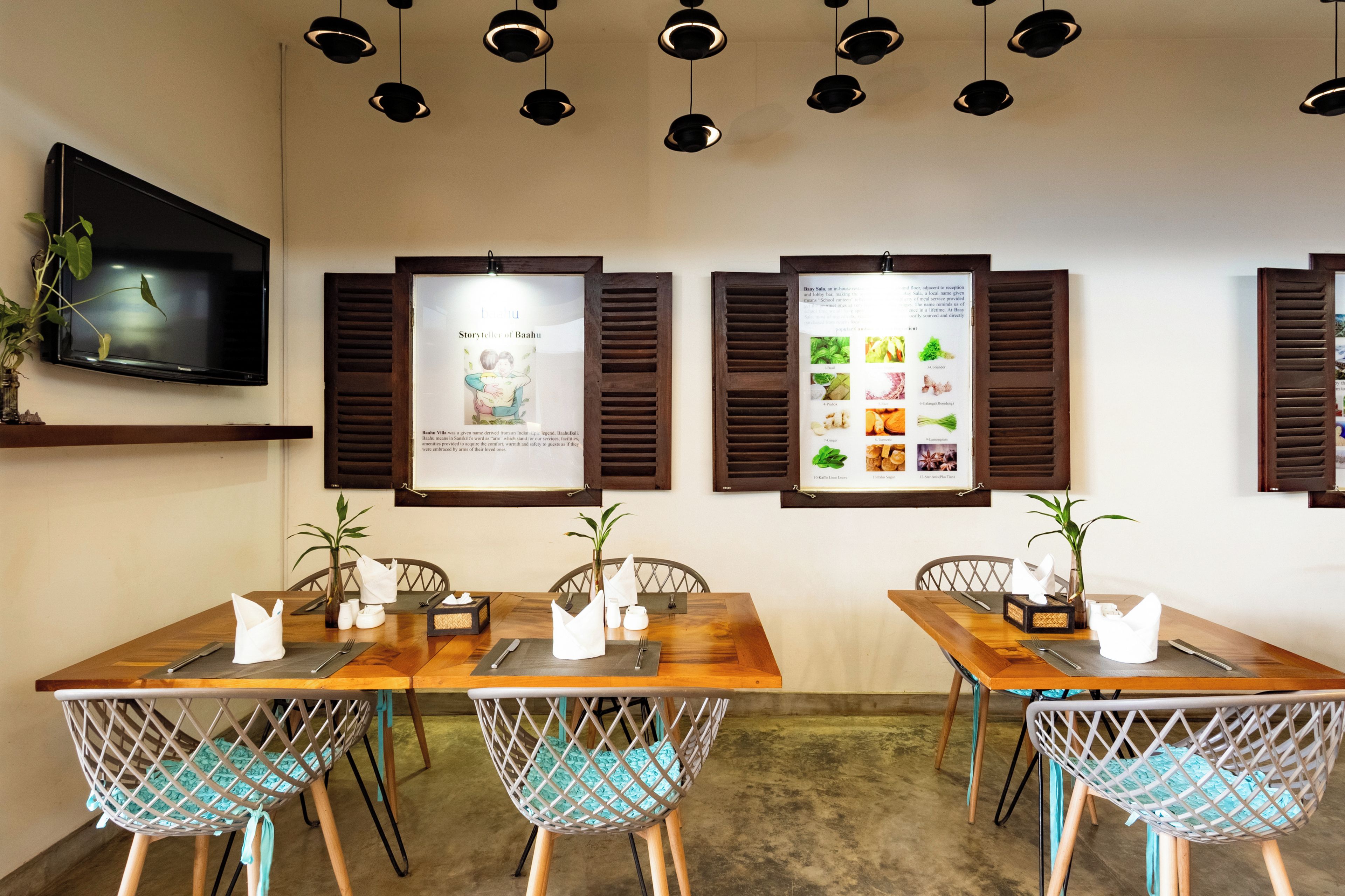 A restaurant with wooden tables and chairs, a flat-screen TV mounted on the wall, and menu boards displaying food items.