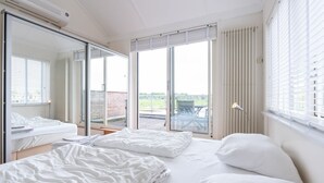Ein Hotelzimmer mit Bett, Schreibtisch, Stuhl, einem großen Fenster mit Jalousien und Blick nach draußen.