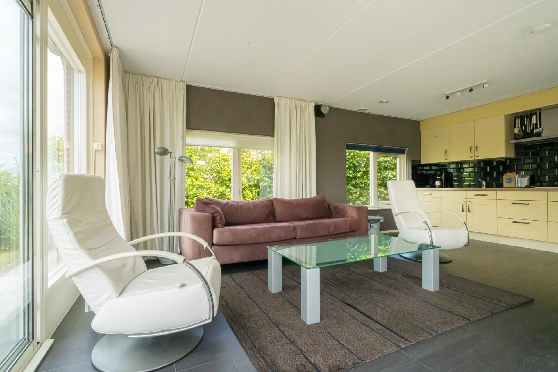A modern living room with a glass coffee table, a sofa, and two armchairs.