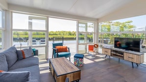 A spacious living area with a sofa, chairs, a coffee table, a TV, and a view of a lake.