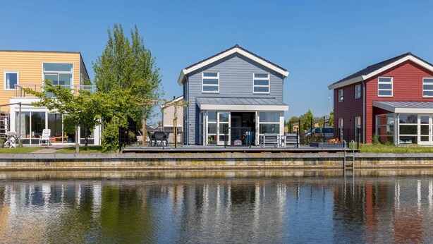 A row of houses by a calm water body, with a clear sky.