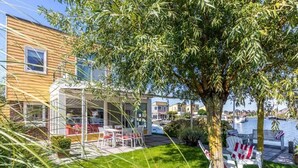 Un edificio moderno con fachada de vidrio, un área verde con asientos al aire libre y un árbol en primer plano.