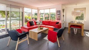Una sala de estar moderna con un sofá rojo, dos sillones blanco y negro, una mesa de centro de madera y un escritorio con una lámpara.