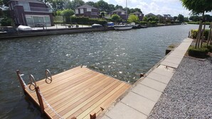 Une jetée en bois s’étendant dans un fleuve paisible, entourée de maisons et sous un ciel dégagé.
