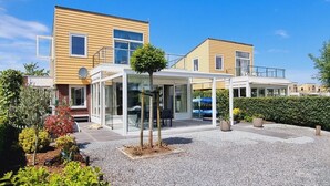 Un immeuble résidentiel moderne doté d’un patio couvert, d’un petit arbre et d’une allée gravillonnée.
