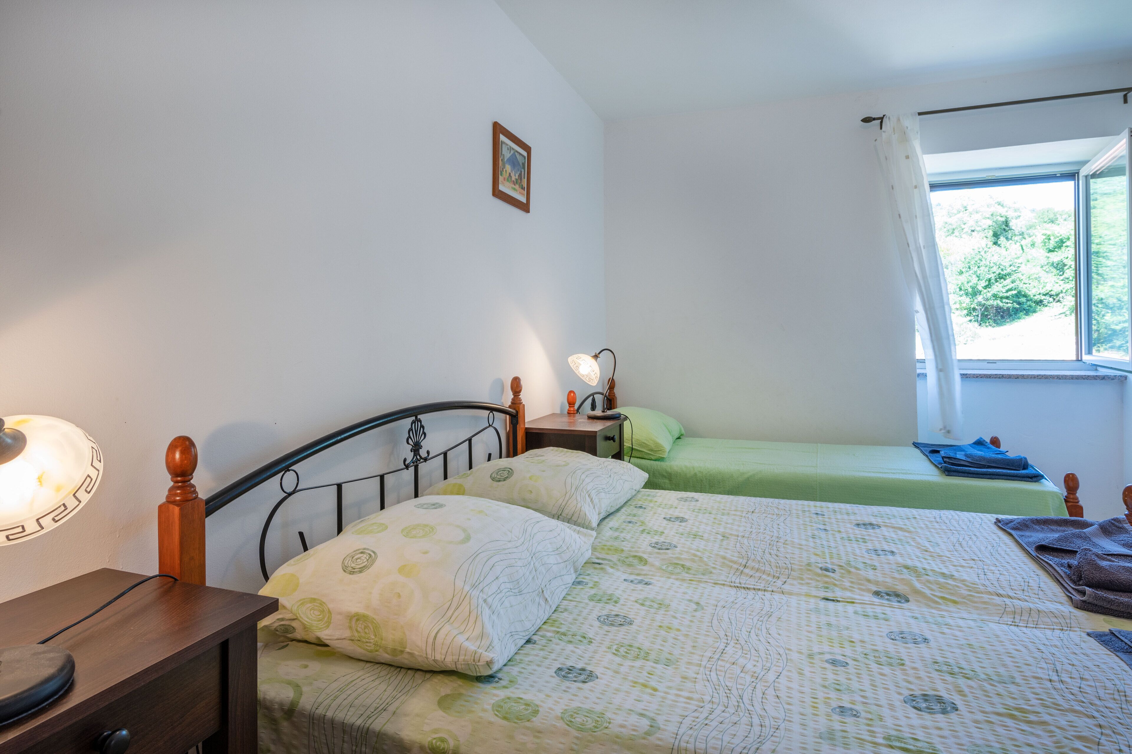 A bedroom with two beds, a bedside table with a lamp, a small bedside table with a lamp, and a window with curtains.